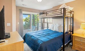 Un dormitorio con literas, un escritorio con computadora, una silla y una ventana con vista a árboles.