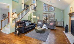 A spacious living room with a staircase, leather sofa, armchairs, and a fireplace. - Serene 5BR Lake House - LAKE VIEW - Gravois Mills (Gravois Mills)