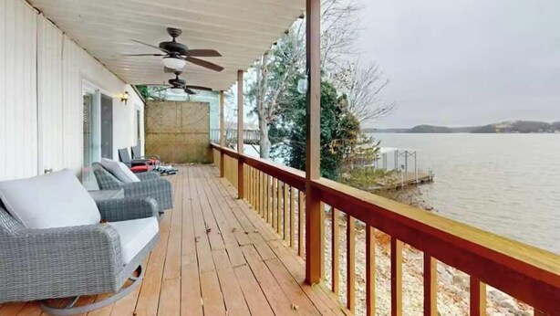 Eine überdachte Terrasse mit Korbmöbeln, einem Deckenventilator und Blick auf einen See.