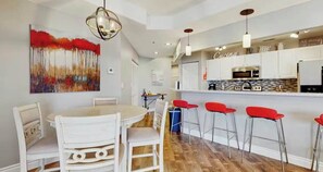 A modern kitchen with white cabinets, a dining area with a round table and white chairs, and a bar area with red stools. - Bright 3BR Condo - LAKE VIEW - Lake Ozark (Lake Ozark)