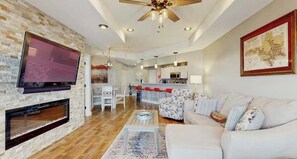 A modern living room with a fireplace, a flat-screen TV, a ceiling fan, and a dining area with red chairs. - Bright 3BR Condo - LAKE VIEW - Lake Ozark (Lake Ozark)