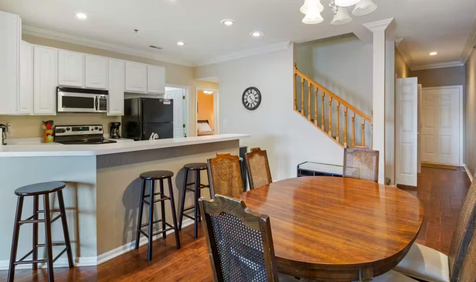 A kitchen with white cabinets, a microwave, a stove, and a refrigerator. There is a dining area with a wooden table and chairs.