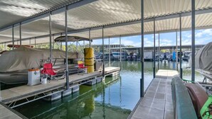 Un muelle cubierto con un bote, una zona de estar techada y vistas a embarcaciones en el agua.