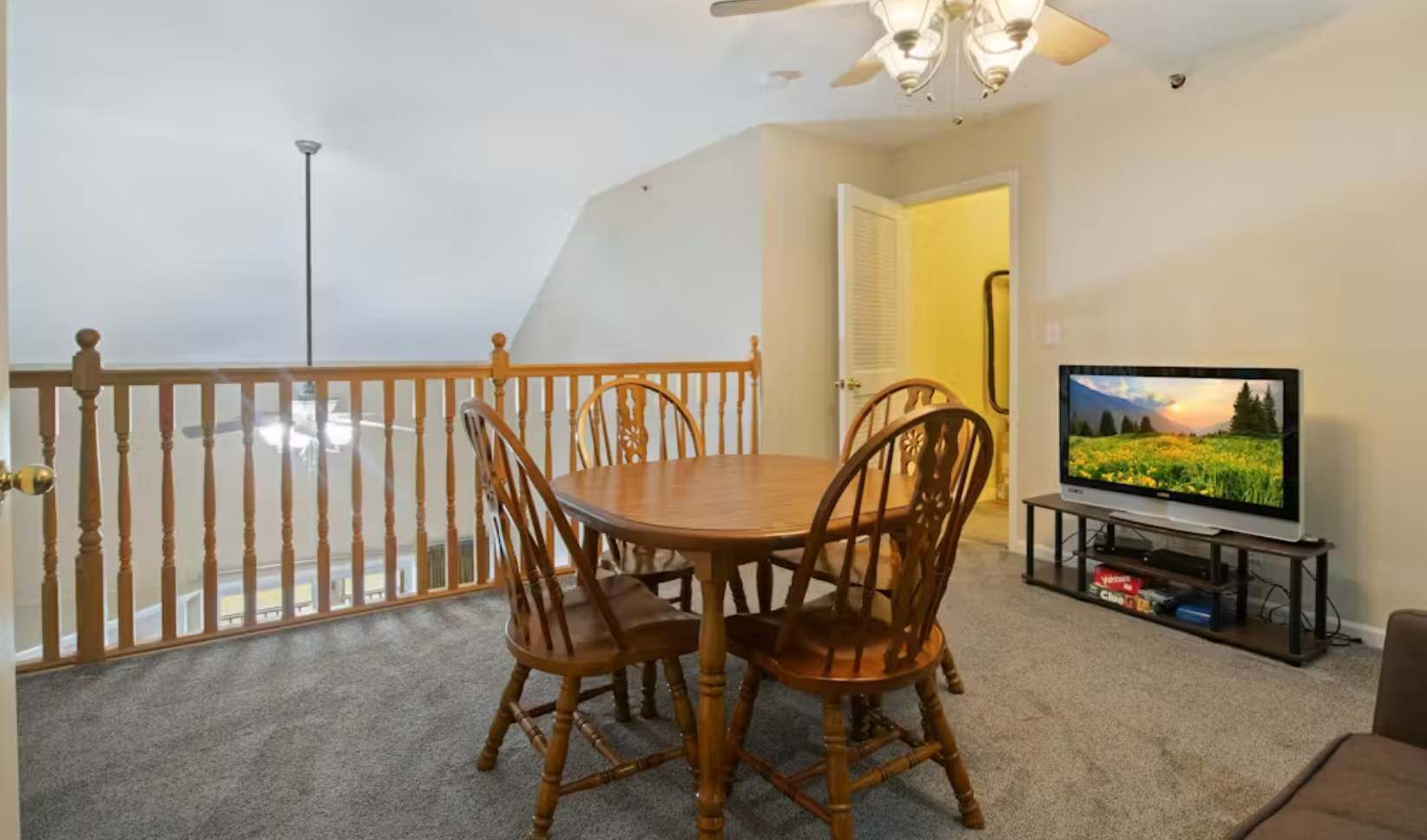 Un balcon avec une balustrade en bois, une table à manger avec des chaises, un téléviseur posé sur un meuble et une porte donnant sur une autre pièce.