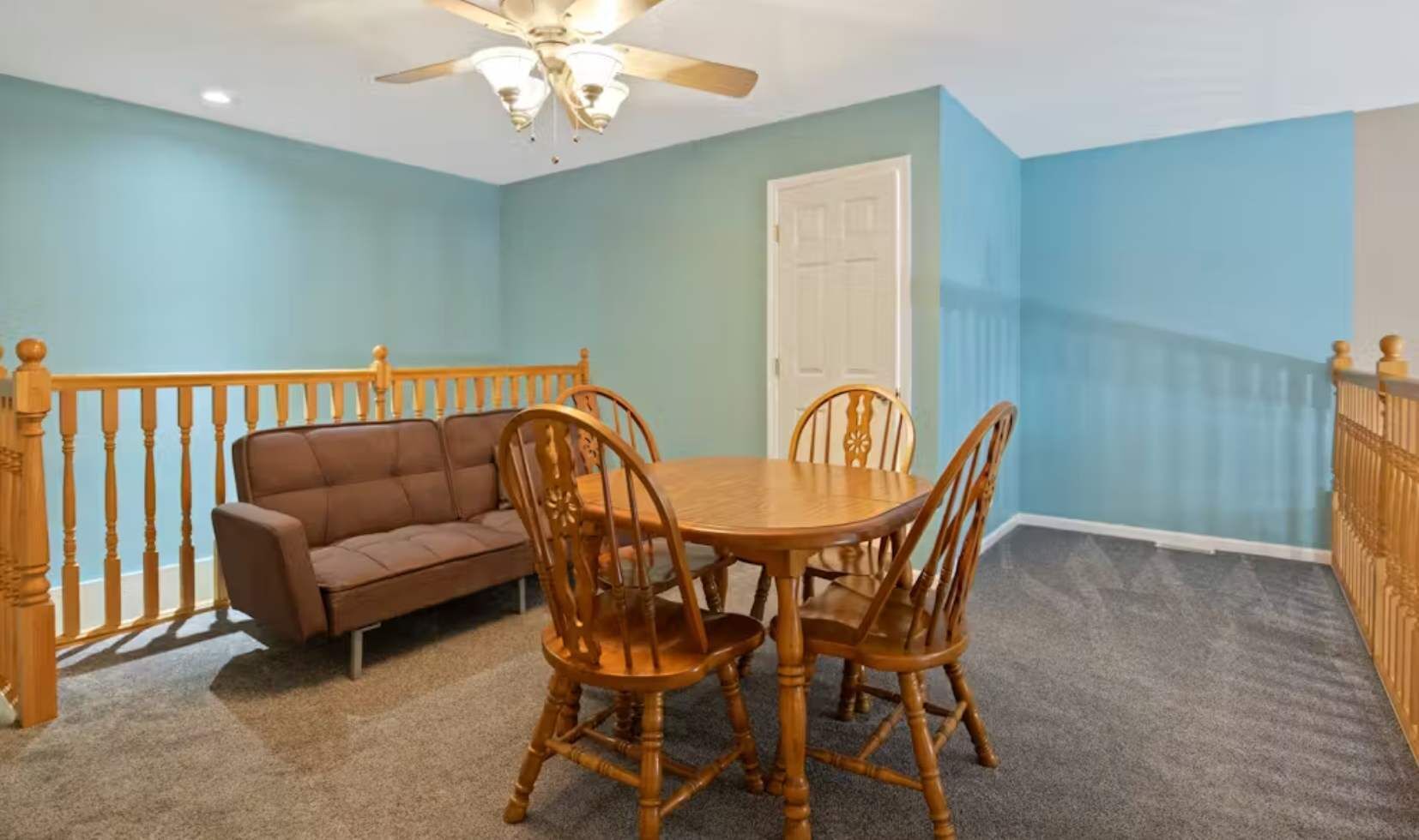 A room with a ceiling fan, a dining table with chairs, a sofa, and a door.