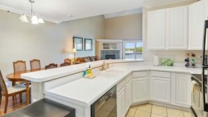 Una cocina moderna con armarios blancos, una isla central y un comedor con sillas de madera.