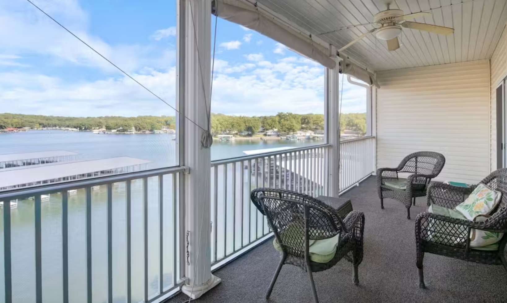 Een balkon met rieten meubels, een plafondventilator en uitzicht op een meer.