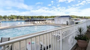Una piscina con cerca blanca, sillas de descanso y un edificio con techo gris al fondo.