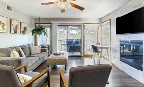 Una sala de estar moderna con un sofá, sillones, una mesa de centro, un ventilador de techo y una televisión grande.
