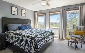Un dormitorio con cama, una silla, una mesita de noche, un ventilador de techo y vistas por la ventana.