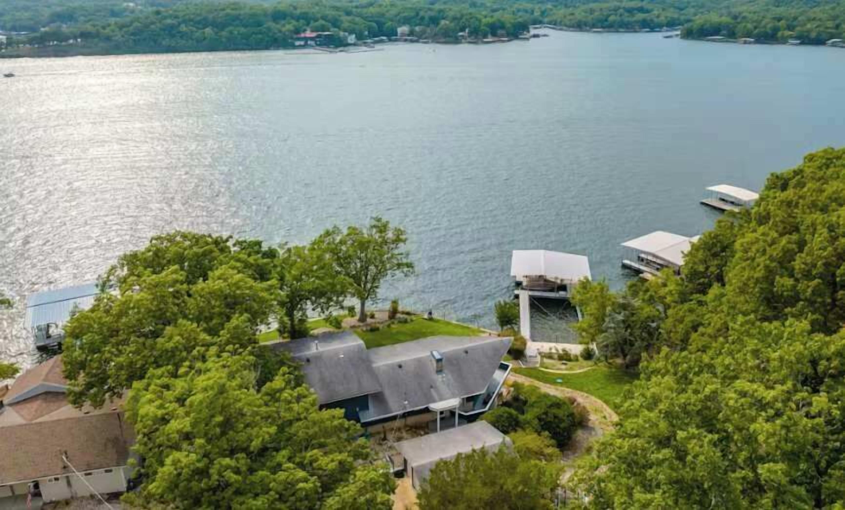 Propiedad frente al lago con una casa moderna, un muelle y vegetación circundante.