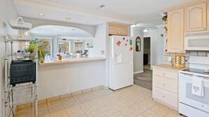 Una cucina con lavastoviglie integrata, mobili bianchi, un frigorifero con calamite e pavimento piastrellato.