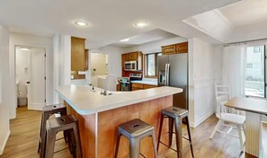 Una cocina moderna con una isla central, taburetes de bar y una zona de comedor con mesa y sillas.