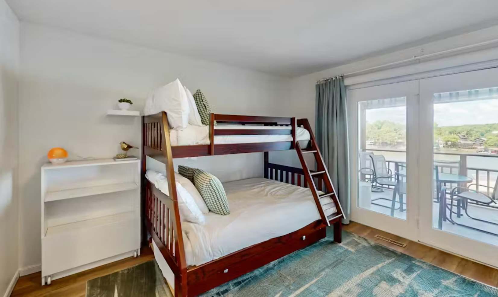 A bunk bed with a ladder, a desk with a chair, and a view of the outdoors through a large window.