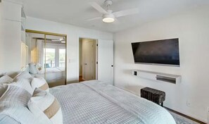 Un dormitorio con cama, televisión montada en la pared y ventilador de techo.