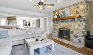 Una sala de estar con chimenea de piedra, un sofá, una mesa de centro y un ventilador de techo.