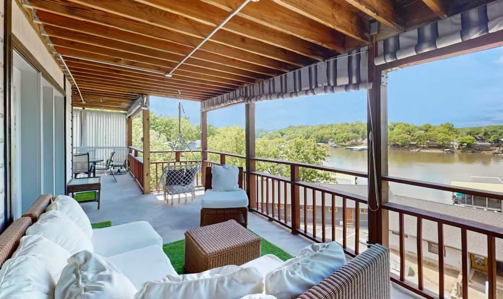 A covered outdoor area with a sofa, chairs, and a view of a lake.