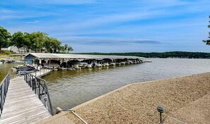 A dock with boats, a covered area, and a pebbled beach. - Serene 2BR Condo - Lake Views - Community Pool (Osage Beach)
