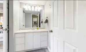 A bathroom with a white vanity, a mirror, and a light fixture above the mirror. - Unwind by the Lake - 2BR Condo - Lakeview Getaway (Osage Beach)