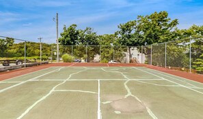 An outdoor tennis court with a net, surrounded by a fence, trees, and a building in the background. - Unwind by the Lake - 2BR Condo - Lakeview Getaway (Osage Beach)
