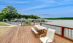 A wooden deck with a table and chairs, overlooking a lake with boats and a dock. - Unwind by the Lake - 2BR Condo - Lakeview Getaway (Osage Beach)