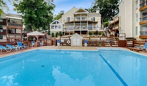 A swimming pool with lounge chairs, a lifeguard stand, and a building with multiple balconies. - Serene 2BR Condo - Lake Views - Community Pool (Osage Beach)