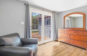 Habitació amb un sofà de pell negra, un moble d'estil antic amb calaixos, un mirall gran i una porta corredissa de vidre que dona a una zona exterior.
