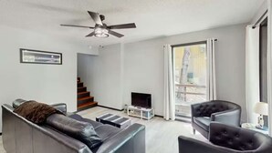 A modern living room with a sofa, armchair, TV, and a ceiling fan. - Charming lakefront Escape with Private Dock, Kayaks, and Beautiful Views (Eldon)