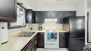 A modern kitchen with dark cabinets, a white stove, and a black refrigerator. - Charming lakefront Escape with Private Dock, Kayaks, and Beautiful Views (Eldon)