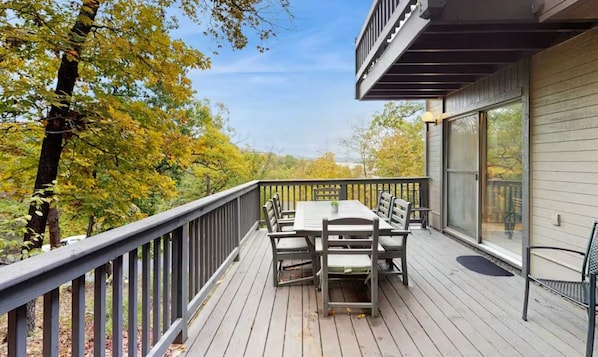 A deck with a table and chairs, overlooking a forested area.
