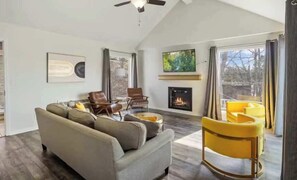 A living room with a fireplace, a sofa, a chair, and a TV. - Serene 3BR House - LAKE VIEW - Margaritaville (Osage Beach)