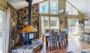 A stone fireplace with a chimney, a dining area with zebra-striped chairs, and a kitchen area with a chandelier.