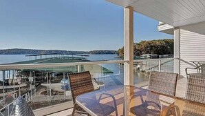 Un balcon avec des fauteuils en osier, une table en verre et une vue sur l’eau et le pont.