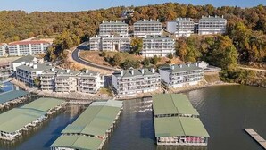 Un hôtel situé au bord de l’eau, composé de plusieurs bâtiments, de quais et adossé à une colline boisée.