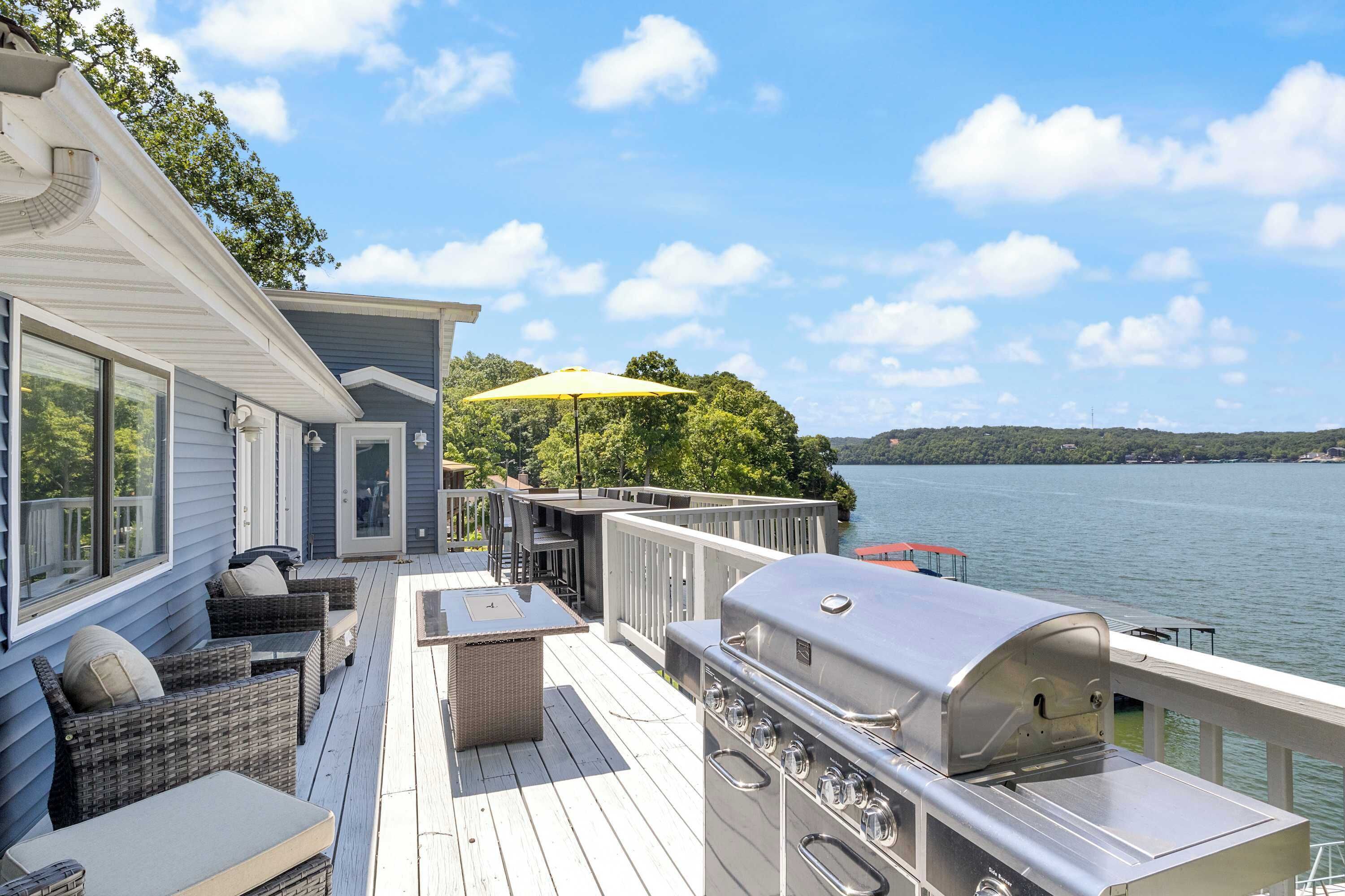 Una terraza con mobiliario exterior, una parrilla y vista a un lago.