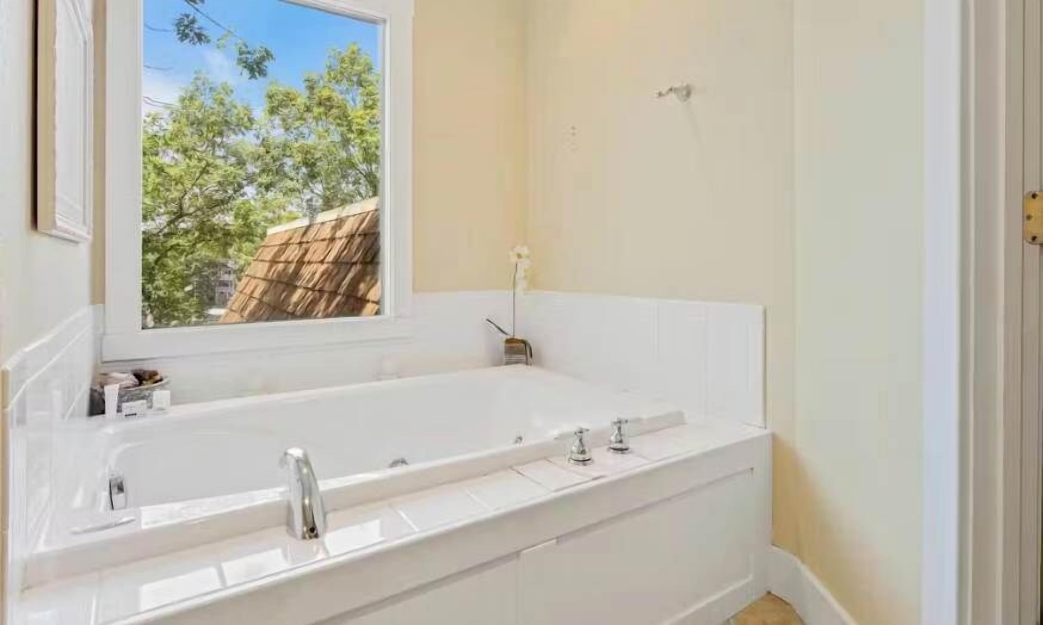 A bathroom with a large bathtub, a window, and a view of trees outside.