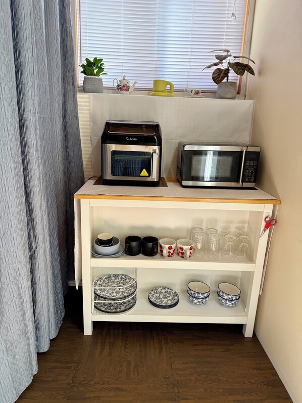 Une petite cuisine équipée d’un four à micro-ondes, d’un grille-pain et d’une étagère contenant de la vaisselle et des tasses.