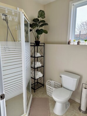 Ein Badezimmer mit Dusche, Toilette, Handtuchhalter, Zimmerpflanze und einem Fenster.