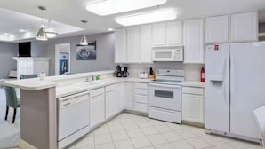 Una cucina moderna con pensili e basi bianche, un forno a microonde integrato, un piano cottura e un frigorifero.