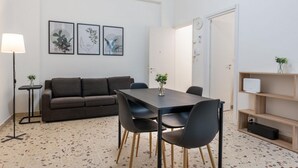 Een moderne woonkamer met een bank, eettafel, stoelen, een lamp, kunst aan de muur en een deur naar een andere kamer.