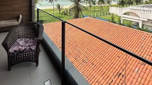 Ein Balkon mit Blick auf einen Strand, Palmen und ein Gebäude mit einem Ziegeldach.
