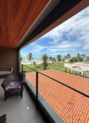 Ein Balkon mit Blick auf einen Strand, Palmen und ein Gebäude mit einem Ziegeldach.