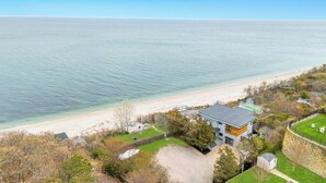 A coastal property with a modern house, a beach, and a stone wall.