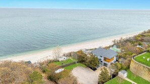 Een landhuis aan de kust met een modern huis, een strand en een stenen muur.