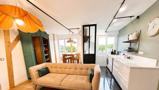 Una cocina moderna con armarios blancos, un comedor con mesa y sillas, y un sofá color beige en la sala.