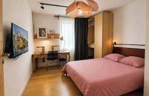 Un dormitorio con una cama, un escritorio con silla, un televisor y un armario.