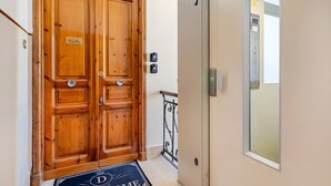 Una porta doppia in legno con un cartello, un tappetino d'ingresso e un ascensore con il pannello di controllo.