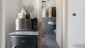 Una cucina compatta con un forno a microonde, un piccolo frigorifero e un vaso con piante essiccate.