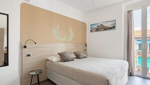 Una camera da letto con un letto, un tavolino, una luce a parete, un termostato e un quadro.
