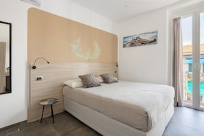 A bedroom with a bed, a small table, a wall-mounted light, a thermostat, and a painting. - Room - Rosmarino with Balcony, Wi-Fi and Air Conditioning (La Spezia)